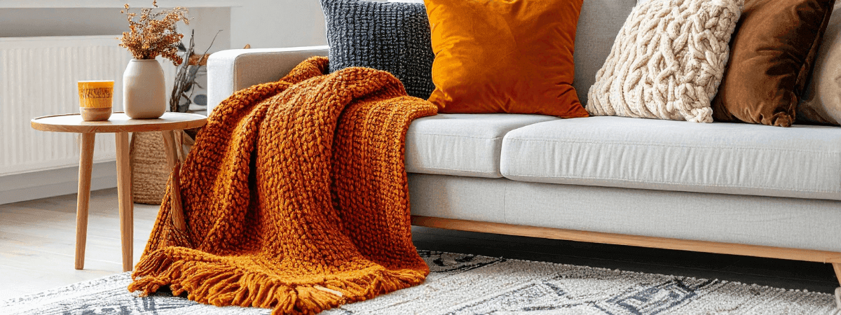 Upholstery care long silver grey sofa with orange cushions and throw by coffee table