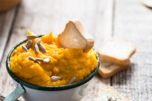 A pumpkin dip snack in a mug with bread croutons and pumpkin seeds on top
